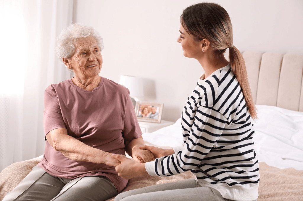 Younger woman and older woman holding hands together on a bed, smiling